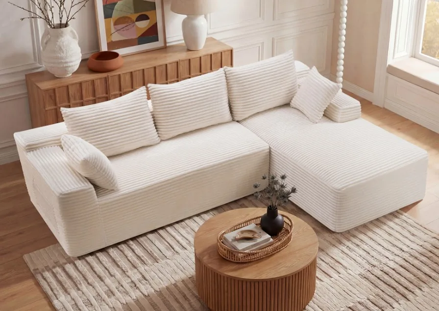 White L-shaped sectional sofa with a round wooden coffee table in a bright living room